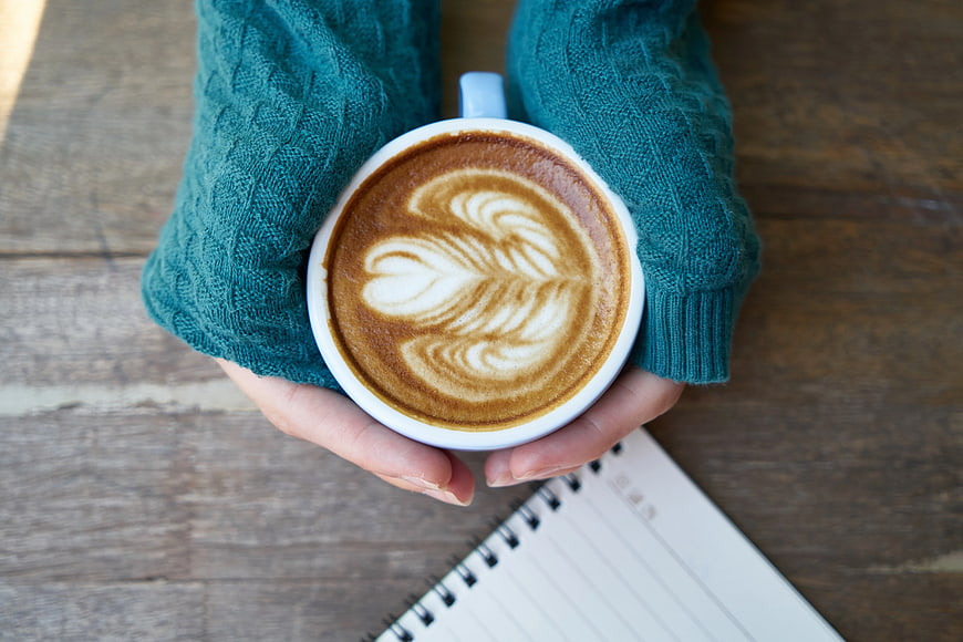 Hands holding latte art coffee cup on wooden table