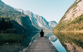 Man meditating on wooden pier in mountain lake