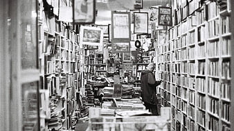 Senior man browsing books in a cluttered black and white bookstore