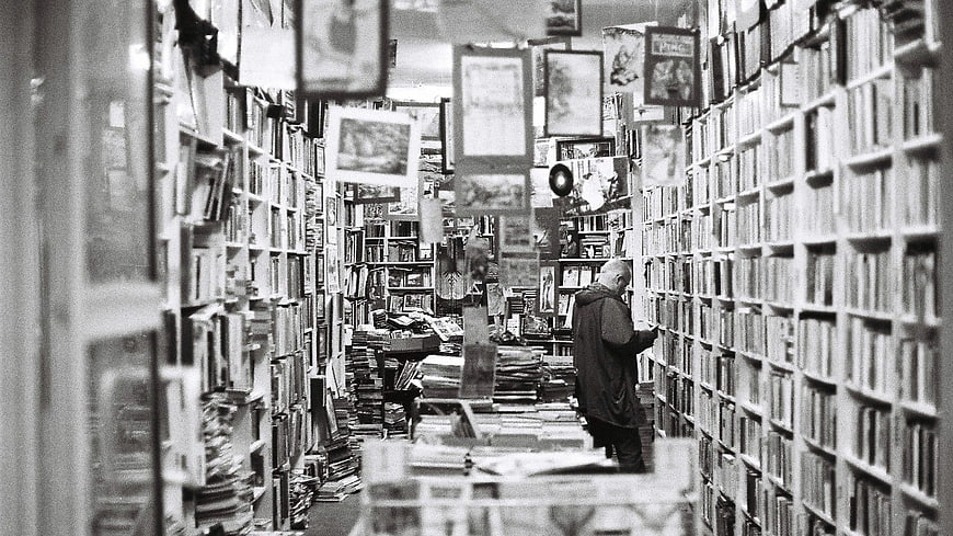 Senior man browsing books in a cluttered black and white bookstore