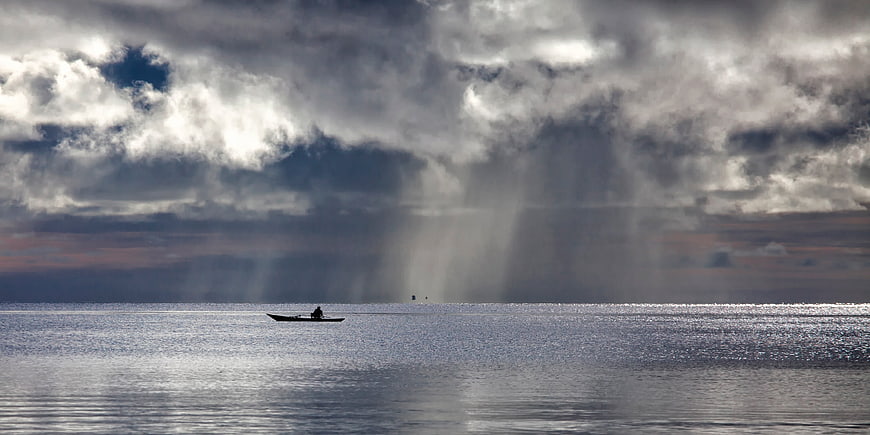 Lone Boat On Calm Sea Under Dramatic Storm Clouds