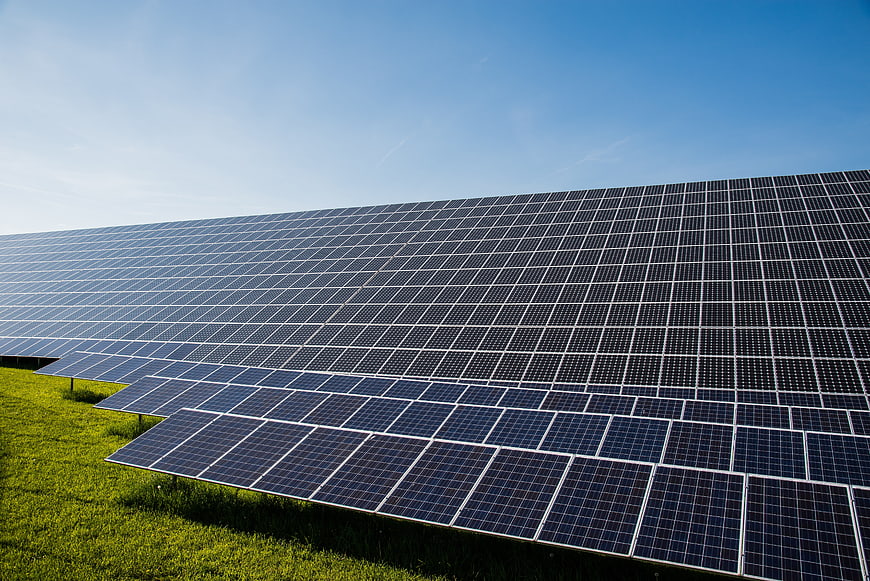 Large solar panel array on green grass under clear blue sky