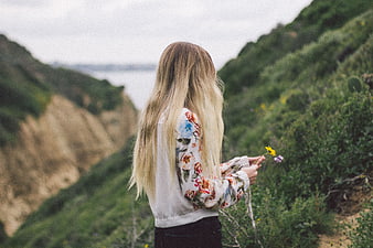 Woman with long blonde hair holding wildflowers on coastal cliff