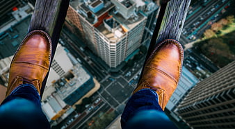First person view of brown boots on high beam over city