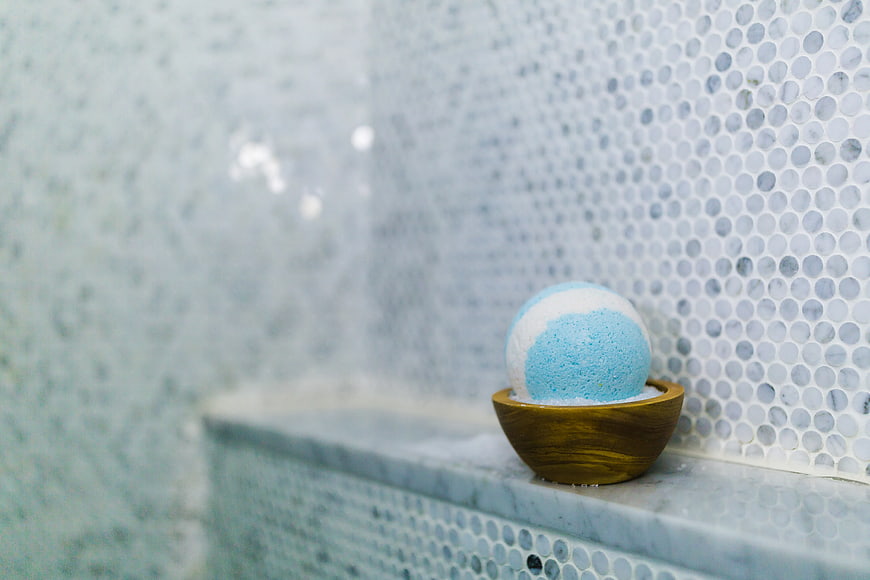 Blue and white bath bomb in wooden bowl on tiled shelf