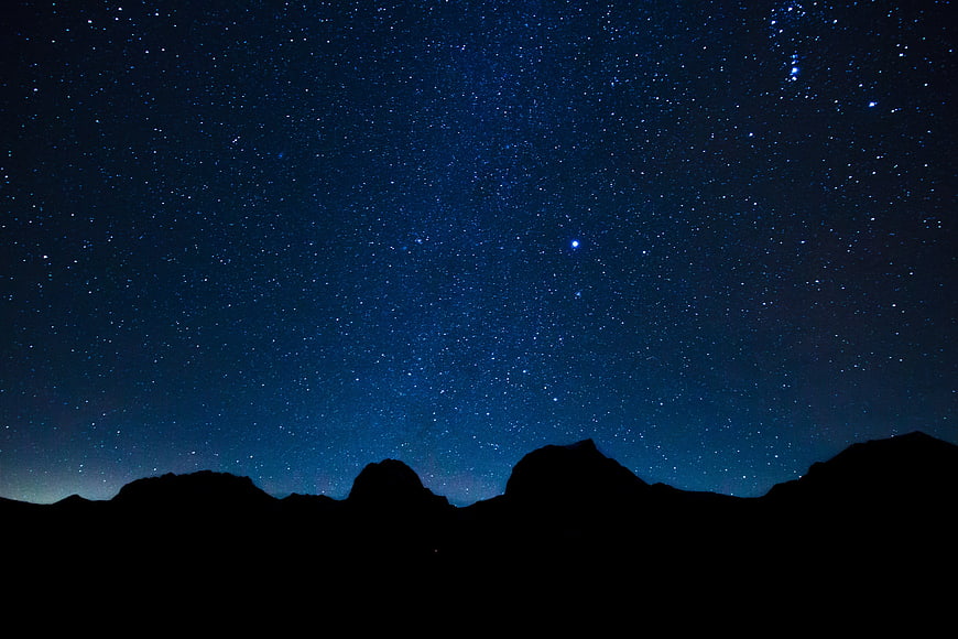 Starry night sky over mountain silhouette landscape