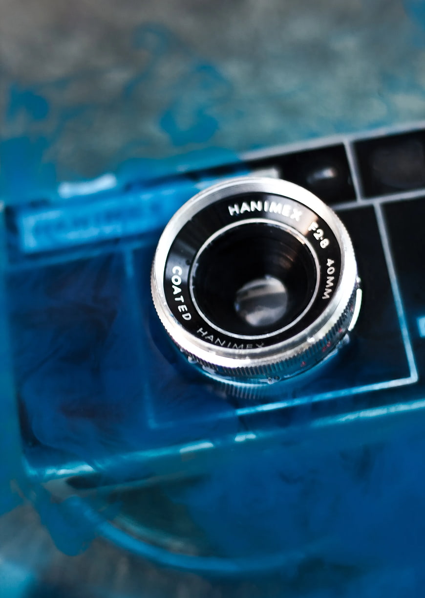 Close-up of vintage Hanimex camera lens submerged in blue water