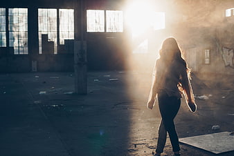 Woman walking in abandoned warehouse with dramatic sunlight
