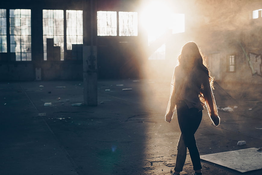 Woman walking in abandoned warehouse with dramatic sunlight