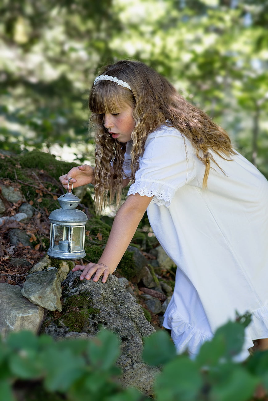 Young Girl in White Dress Holding Lantern in Forest