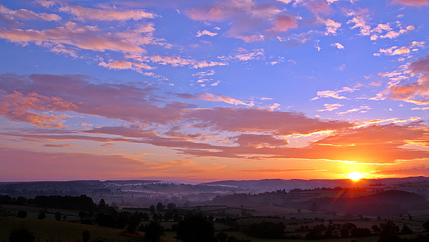 Vibrant Sunrise Over Rolling Hills and Misty Valley