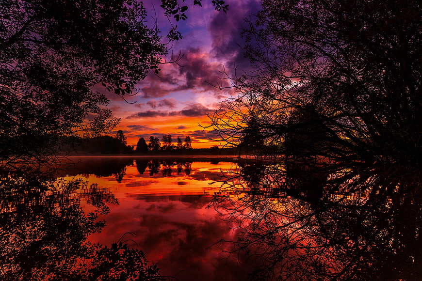 Vibrant purple and orange sunset reflecting on a calm lake