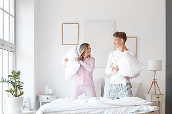 Happy young couple having playful pillow fight in bright bedroom