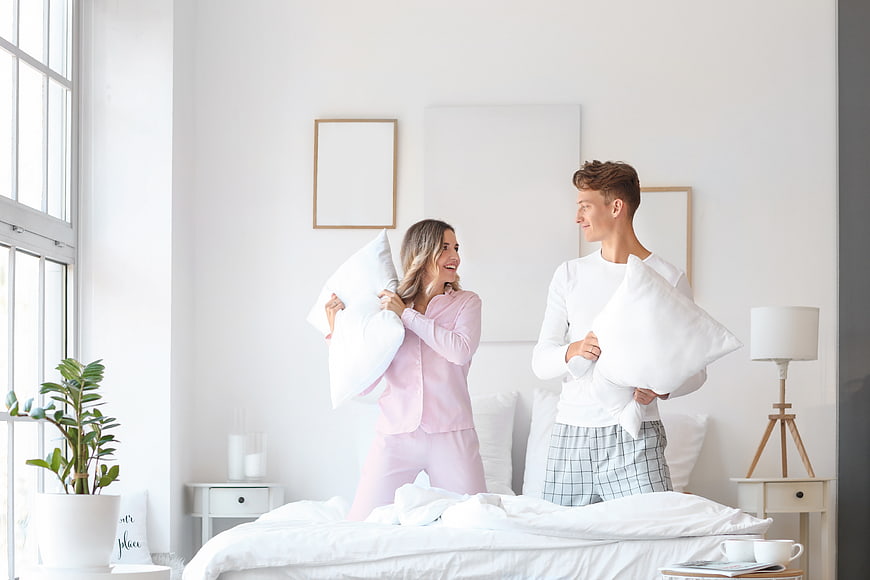 Happy young couple having playful pillow fight in bright bedroom