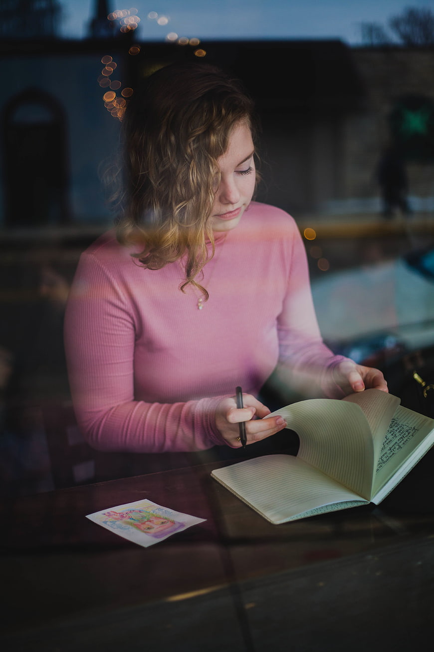 Young woman writing in notebook at cafe window