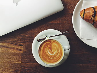 Flat lay of latte art coffee, croissant, and laptop on wooden table