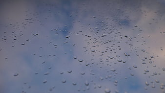 Raindrops on glass window with blurred cloudy sky background