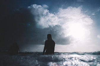 Silhouette of woman in ocean waves with dramatic sky