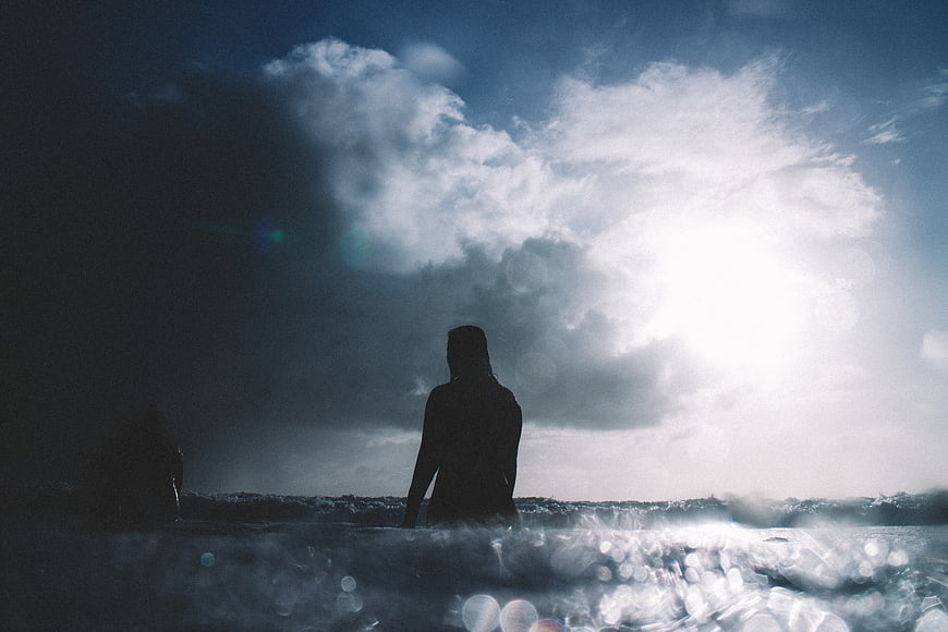 Silhouette of woman in ocean waves with dramatic sky