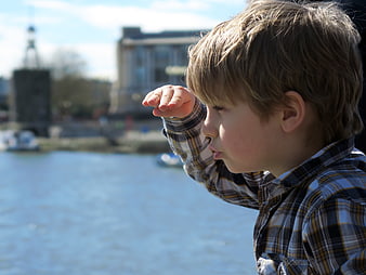 Young boy in plaid shirt looking out over a sunny harbor