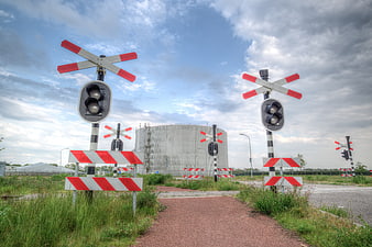 Railway crossing with red and white signals and industrial tank