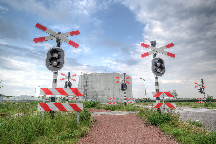Railway crossing with red and white signals and industrial tank