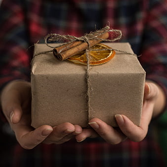 Hands holding rustic kraft paper gift box with cinnamon and dried orange