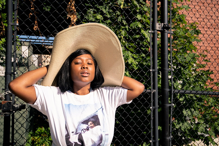 Woman in oversized hat relaxing against chain link fence
