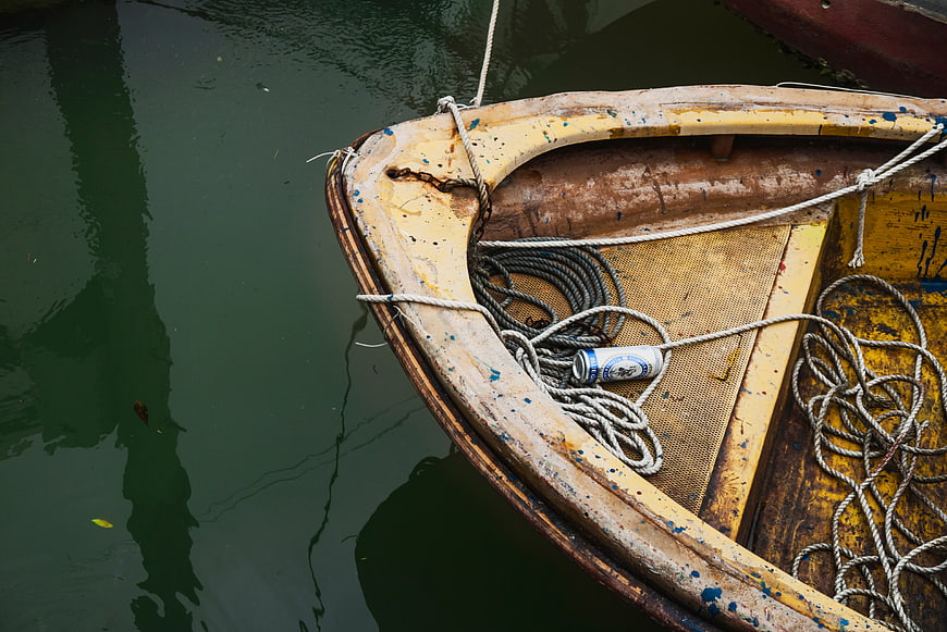 Weathered yellow boat with ropes and can on water