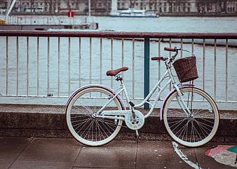 White bicycle with basket parked by river railing