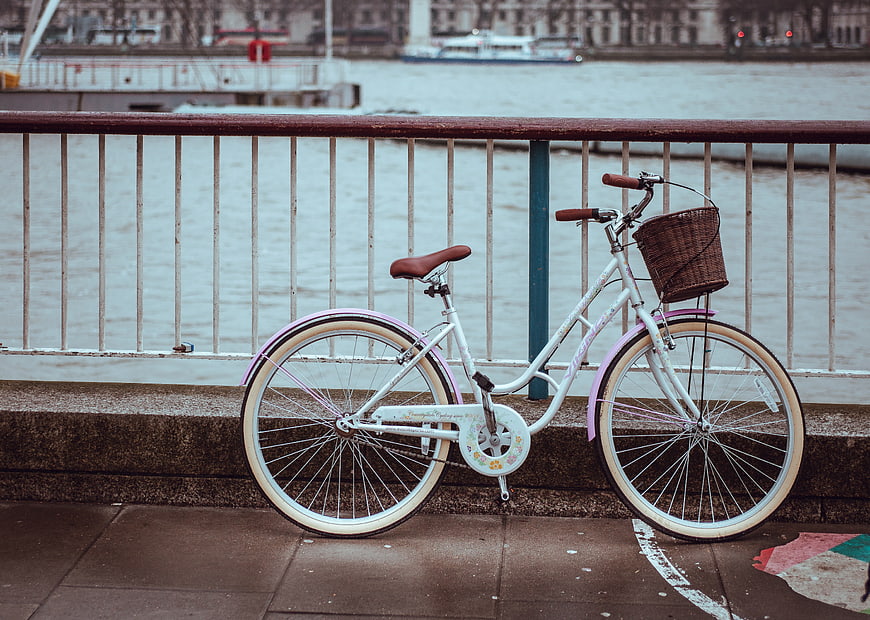 White bicycle with basket parked by river railing