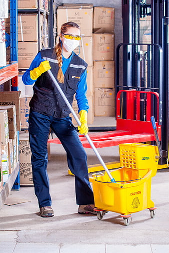 Female warehouse worker mopping floor with yellow mop bucket