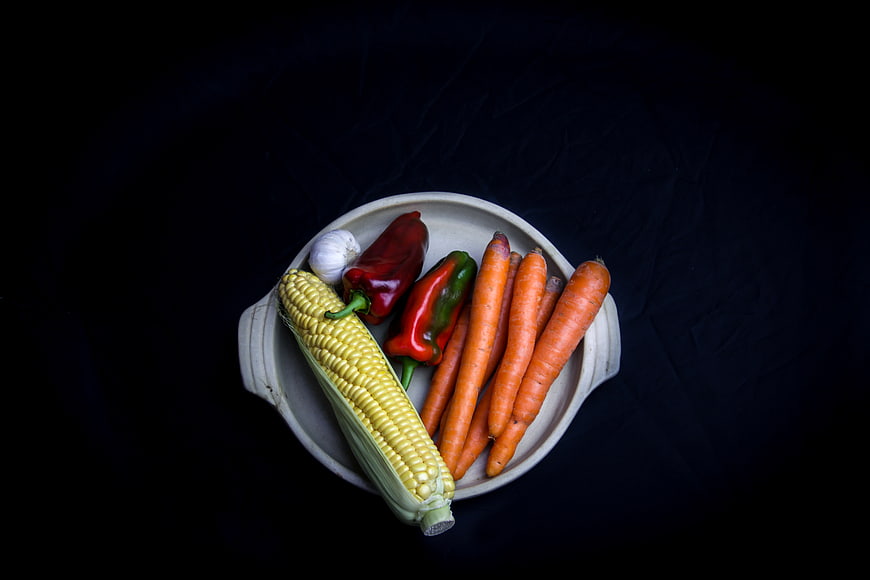 Fresh raw vegetables in a ceramic bowl on black background