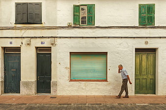 Senior man walking past rustic white building with green shutters