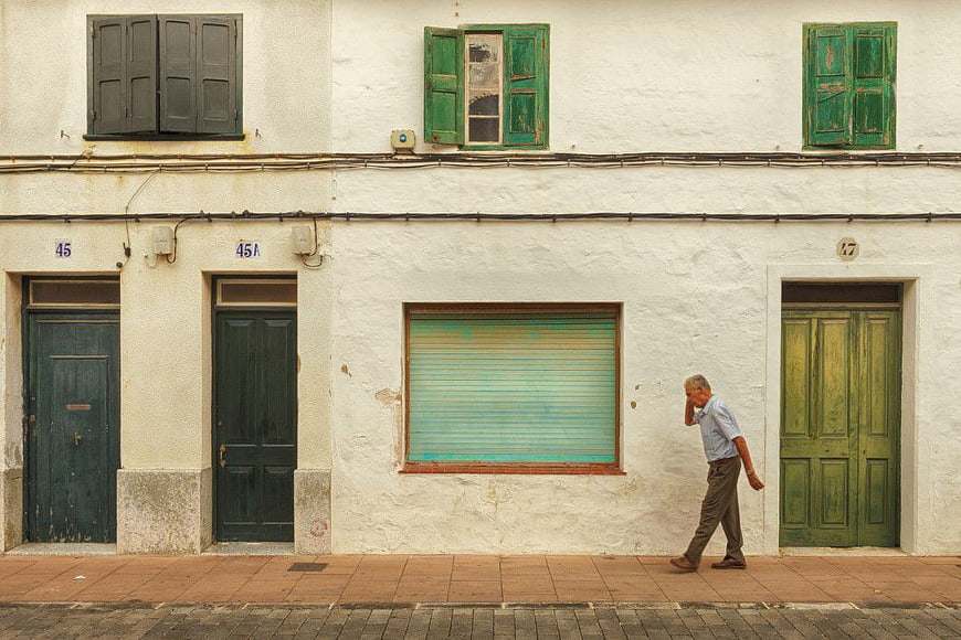 Senior man walking past rustic white building with green shutters