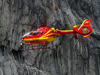 Red and yellow rescue helicopter flying near rocky cliff