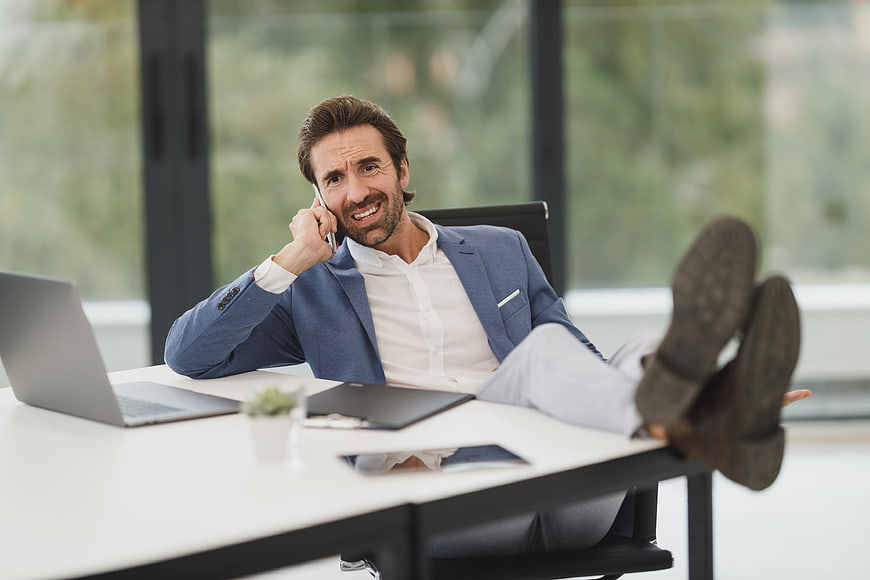 Stressed businessman talking on phone with feet on desk