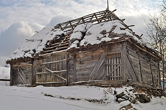 Abandoned wooden barn with snow-covered thatched roof in winter