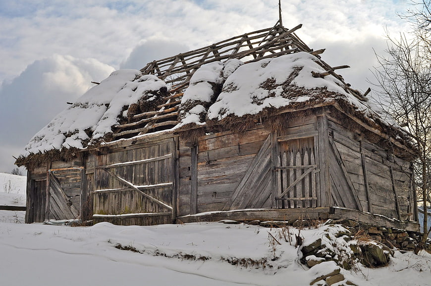 Abandoned wooden barn with snow-covered thatched roof in winter