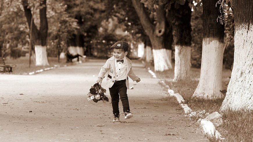 Toddler boy running in park with bouquet of flowers
