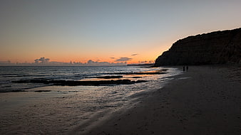 Silhouetted Beach Sunset with Coastal Cliffs and Walking Figures