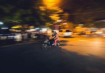 Motion blur of couple riding motorcycle on city street at night