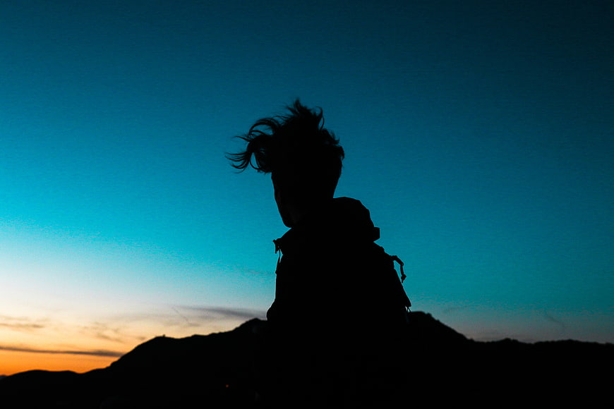 Silhouette of Hiker with Backpack Against Blue Sunset Sky