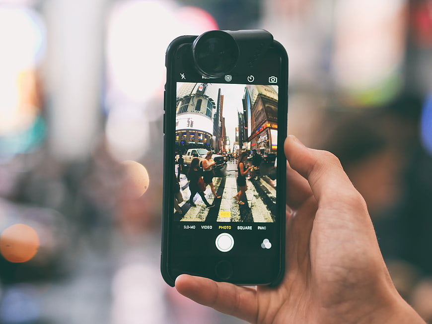Hand holding smartphone with fisheye lens taking photo of city street