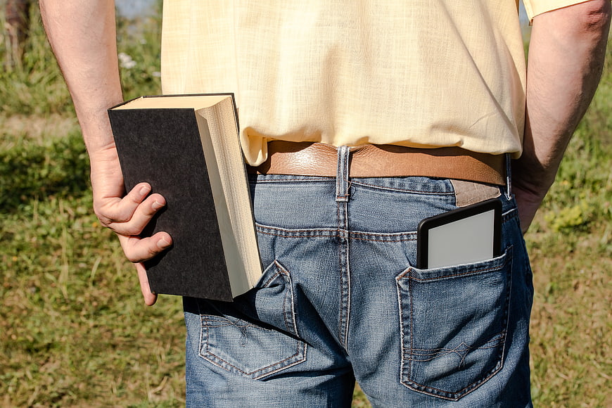 Man holding physical book with e-reader in back pocket
