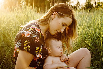 Mother holding baby in grassy field at golden hour