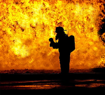 Silhouette of firefighter holding baby against massive fire explosion