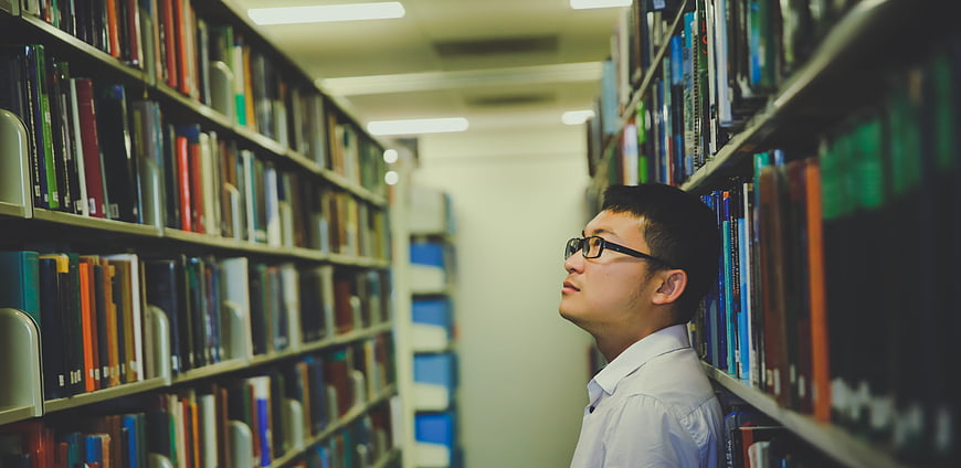 Man looking at books in a library aisle