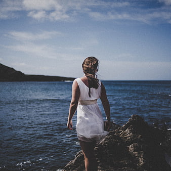 Woman in White Dress Standing on Rocky Coastline