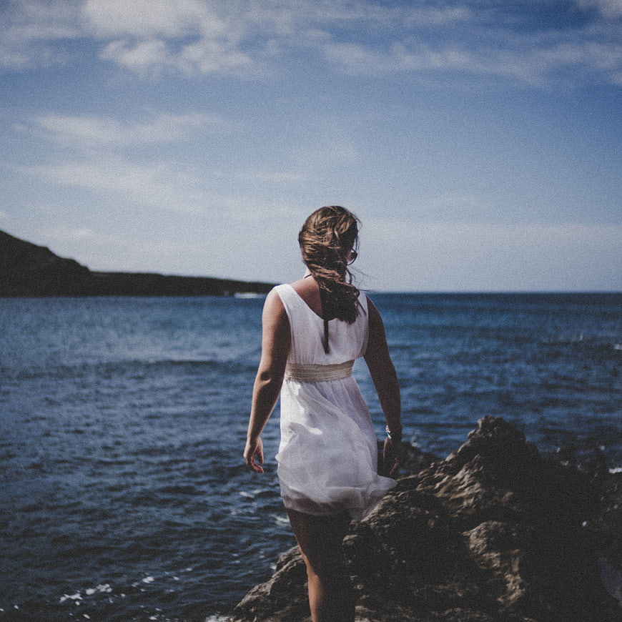 Woman in White Dress Standing on Rocky Coastline